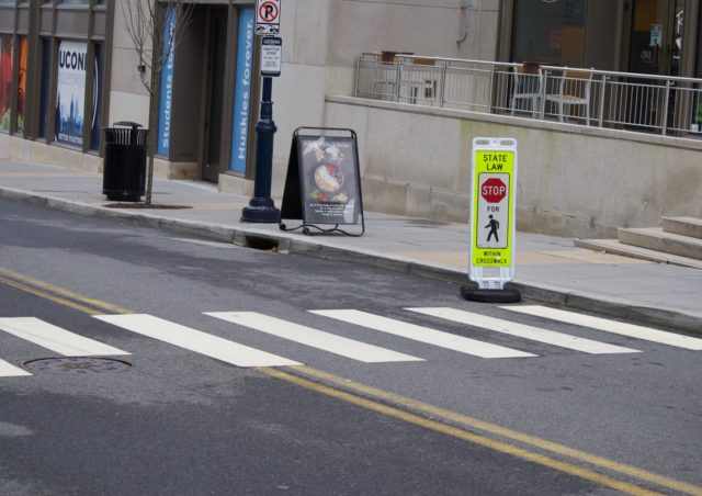 A yield-to-pedestrian sign placed in the gutter instead of on the center yellow line as intended