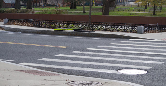A yield-to-pedestrian sign broken and laying down on a sidewalk near crosswalk to popular park