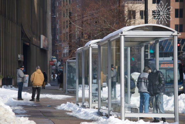 Multiple people on sidewalk and in bus shelter
