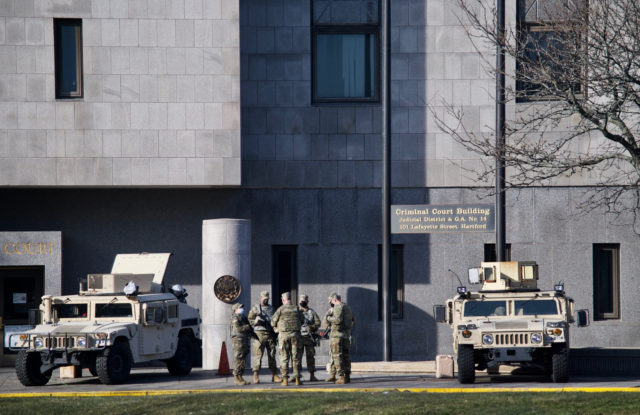 Soldiers standing between two military vehicles outside of Criminal Court