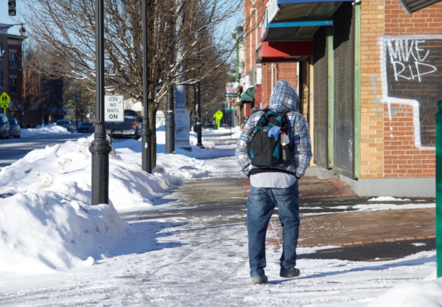 Person wearing backpack, walking on sidewalk
