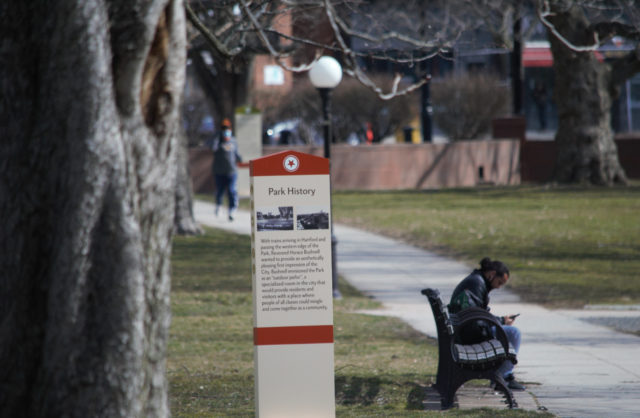 Person sitting on park bench while another jogs nearby