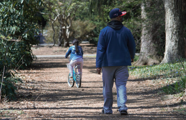 Girl on bike, father walking behind