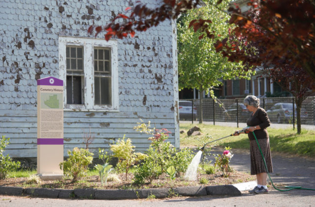 Woman watering flowers and other plants outside a cemetery building