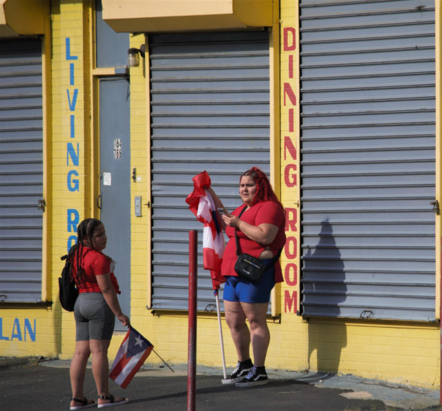 People in red shirts, holding flags, in front of a building painted bright yellow