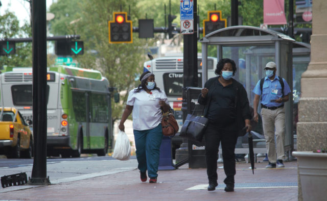 People wearing masks walking near bus stops