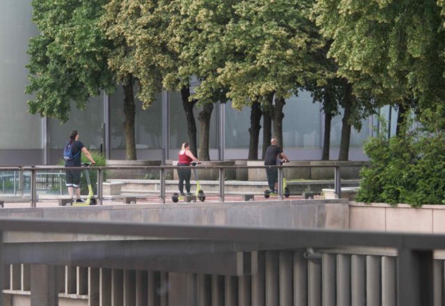 Three people riding electric scooters on Constitution Plaza