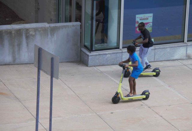 Two people riding e-scooters near Science Center