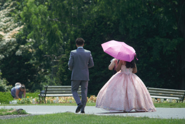 Two people walking, one in gray suit, the other in a pale pink, sparkling dress with a hoop skirt